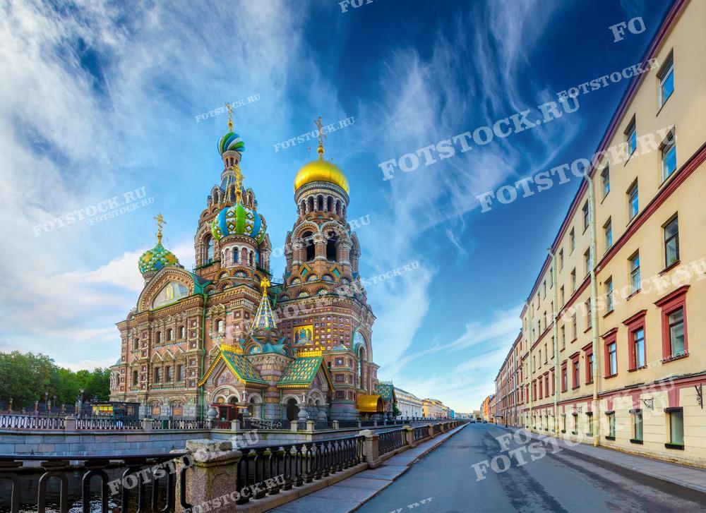 На фотографии изображен Храм Спаса на Крови в Санкт-Петербурге в ясный летний день. Видна набережная канала Грибоедова и окружающие здания. Фото может использоваться для туристических буклетов, открыток и рекламных материалов.